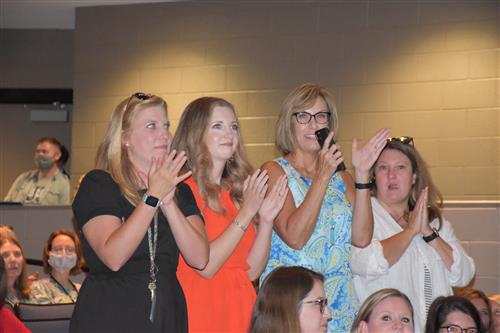 Four teachers smiling and clapping in audience